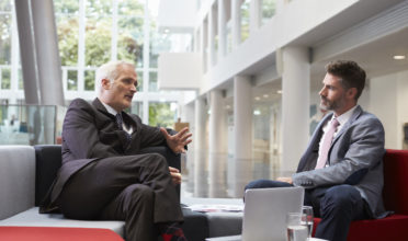 Two Businessmen Meeting In Lobby Area Of Modern Office Two Businessmen Meeting In Lobby Area Of Modern Office